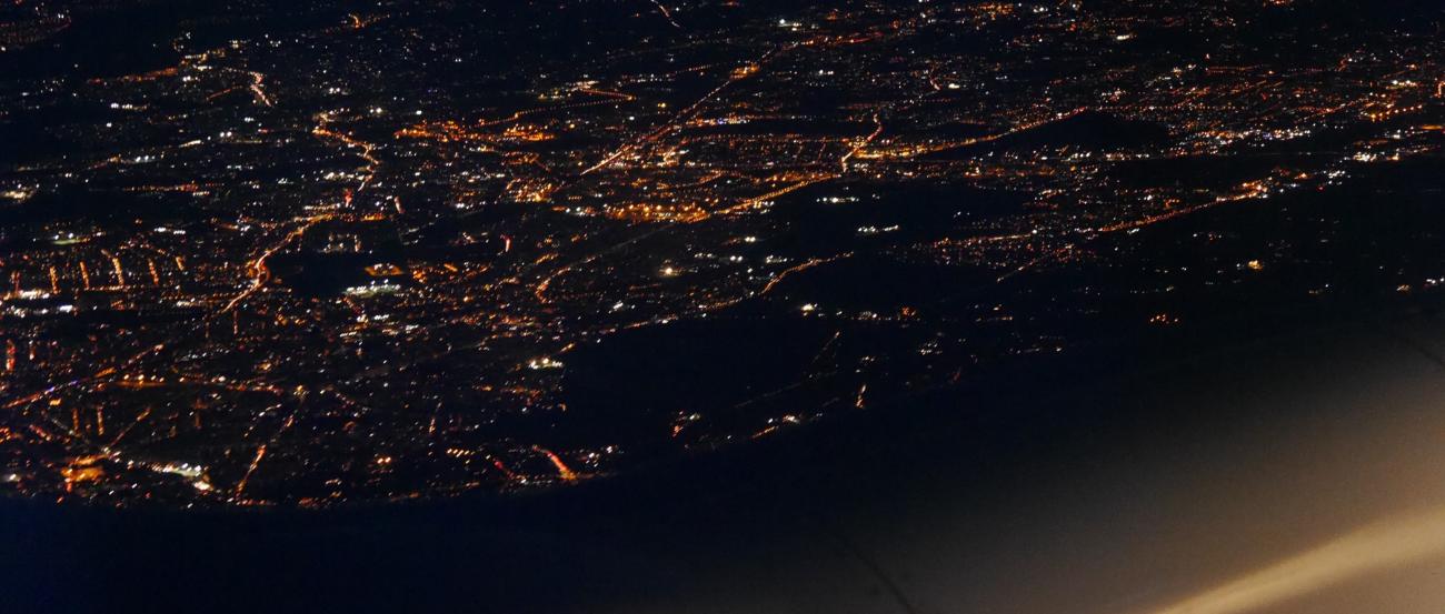 Blick aus einem Flugzeug bei Nacht auf die Lichter einer großen Stadt