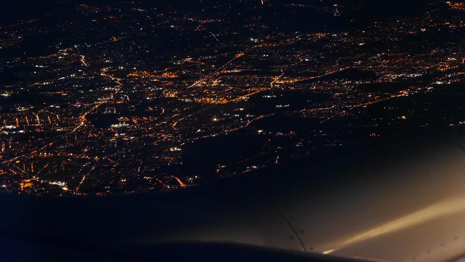Blick aus einem Flugzeug bei Nacht auf die Lichter einer großen Stadt