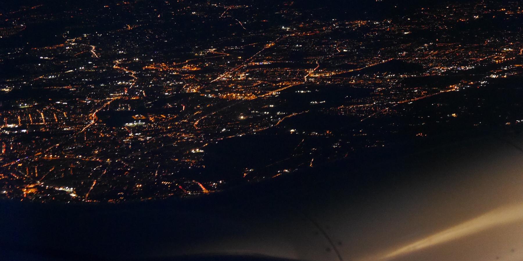 Blick aus einem Flugzeug bei Nacht auf die Lichter einer großen Stadt