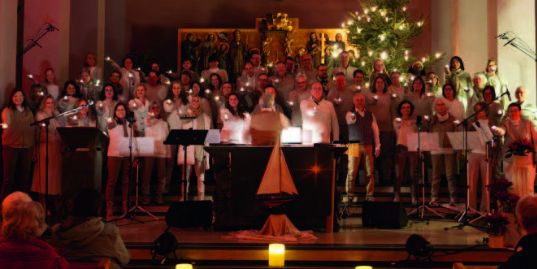 Ein großer Chor steht zusammen im Altarraum, jeder hält eine Kerze in der Hand