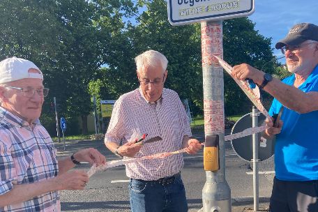 Drei Mitglieder der Kolpingsfamilie Neuwied entfernen Aufkleber von einem Verkehrsstraßenschild