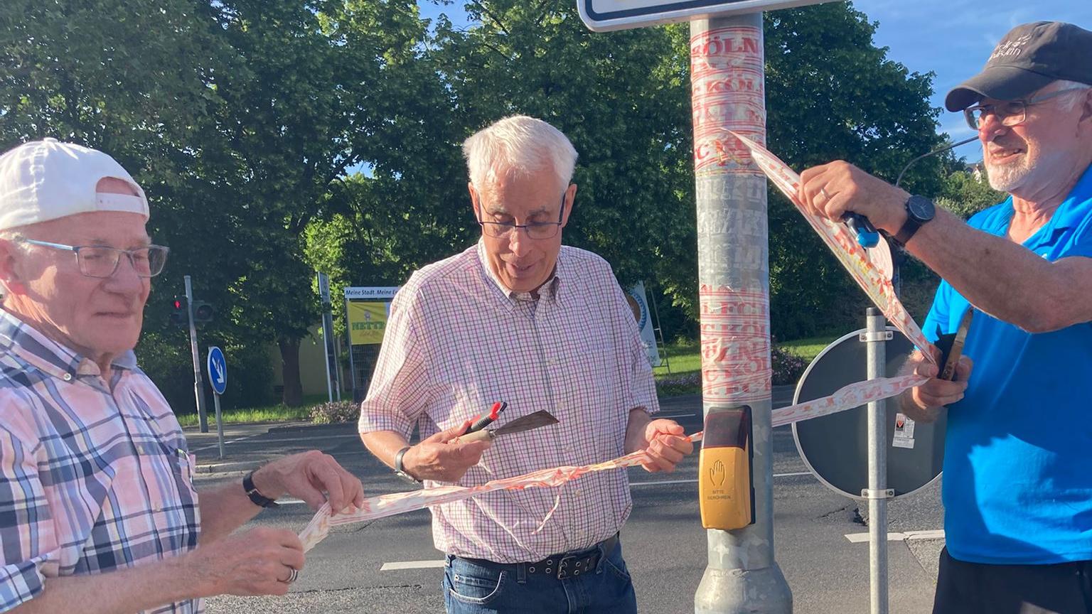 Drei Mitglieder der Kolpingsfamilie Neuwied entfernen Aufkleber von einem Verkehrsstraßenschild