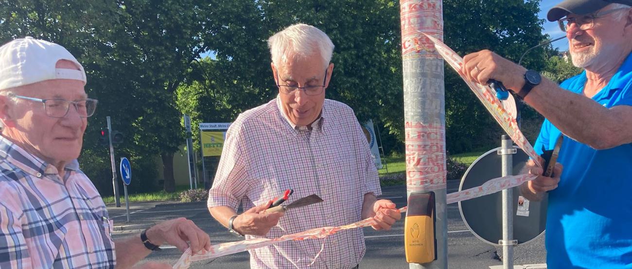 Drei Mitglieder der Kolpingsfamilie Neuwied entfernen Aufkleber von einem Verkehrsstraßenschild