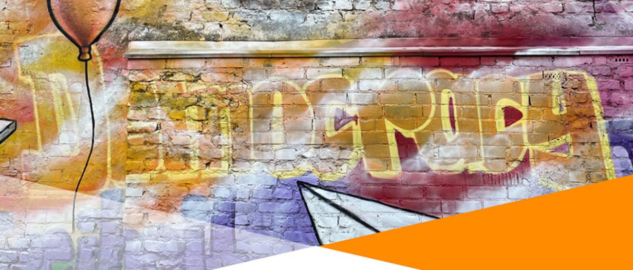 Bild einer bunt besprühten Ziegelmauer mit dem Schriftzug Democracy
