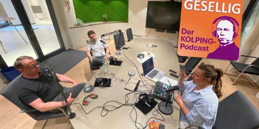 Zwei Männer und eine Frauen sitzen an einem Tisch, es ist viel Aufnahme Technik zu sehen. Sie unterhalten sich