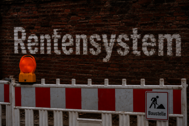 Das Bild zeigt eine Mauer mit dem Schriftzug Rentensystem, davor steht eine Baustellenabsperrung.