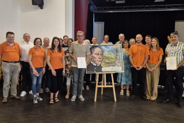 Menschen stehen links und rechts von einem Kolping-Bild, zwei Mitglieder werden für langjährige Mitgliedschaft ausgezeichnet