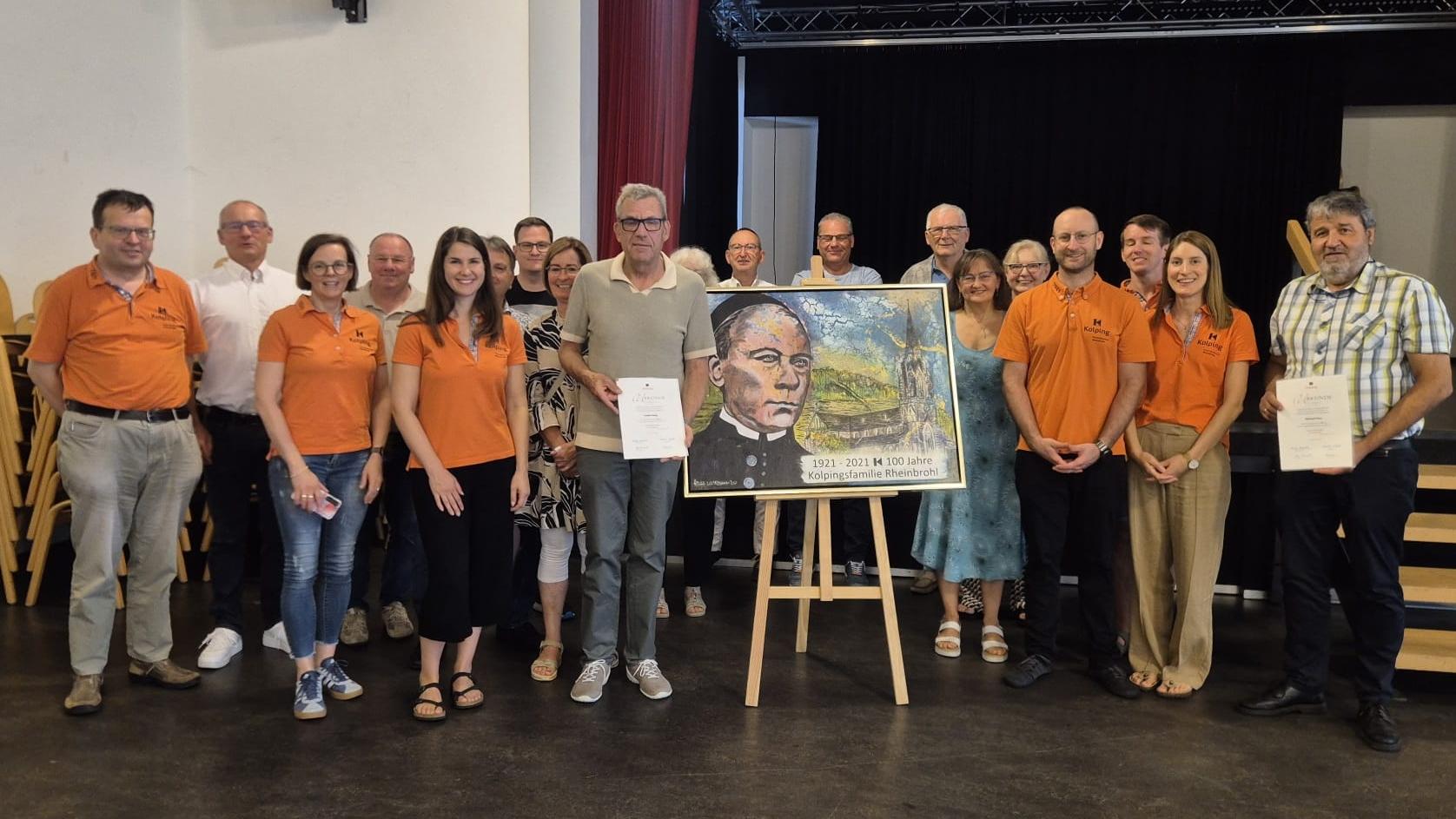 Menschen stehen links und rechts von einem Kolping-Bild, zwei Mitglieder werden für langjährige Mitgliedschaft ausgezeichnet