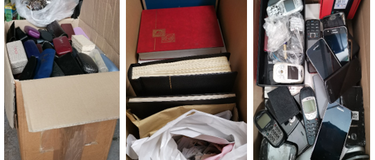 Kartons mit gesammelten Brillen, Briefmarkenalben und Handys