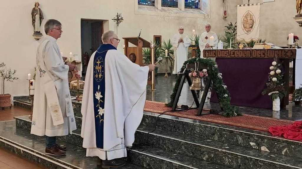 Pastor und Diakone stehen im Altarraum und segnen die neue Glocke