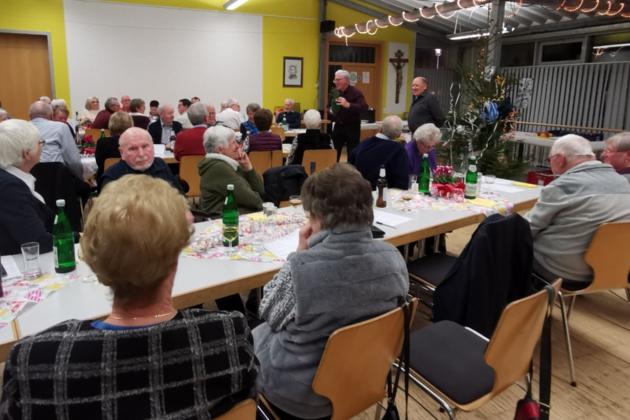 Menschen sitzen gemütlich im Pfarrheim und beteiligen sich an der Versteigerung