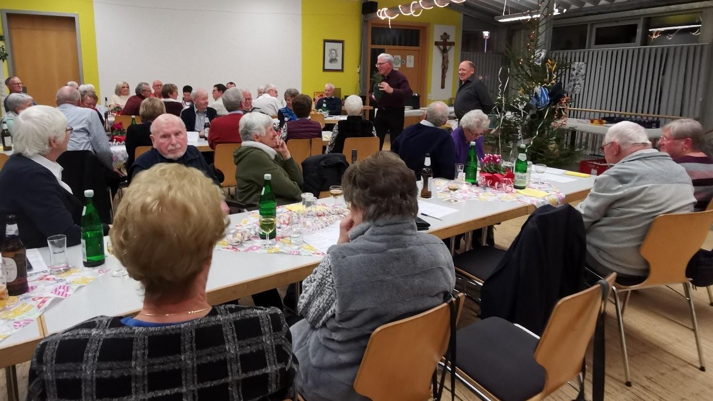 Menschen sitzen gemütlich im Pfarrheim und beteiligen sich an der Versteigerung