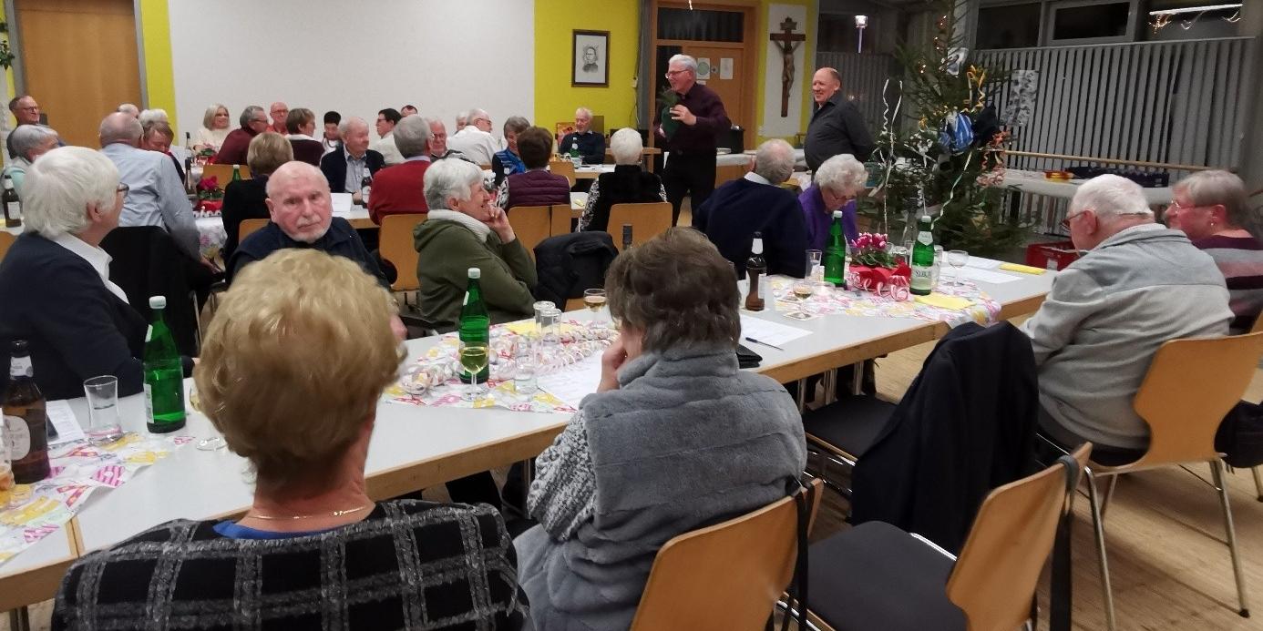 Menschen sitzen gemütlich im Pfarrheim und beteiligen sich an der Versteigerung