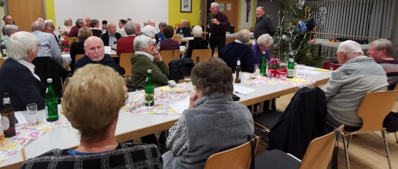 Menschen sitzen gemütlich im Pfarrheim und beteiligen sich an der Versteigerung