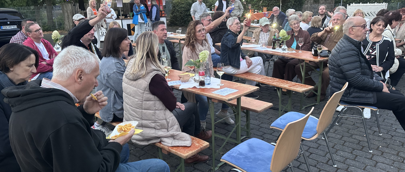 Menschen sitzen draußen auf Bierbänken, hören Musik, sind am Essen und haben eine gute Zeit