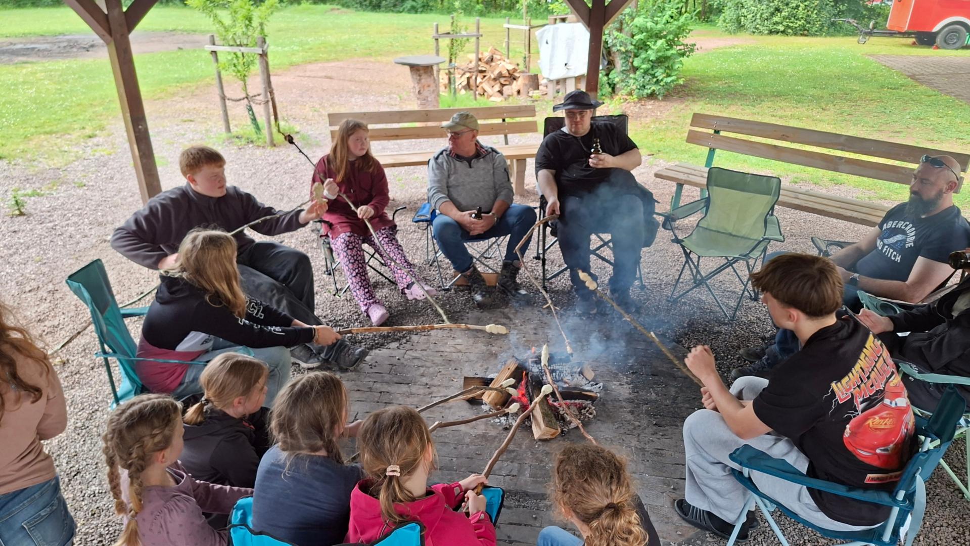 Kinder und Jugendliche sitzen mit Vätern und Großvätern um ein Feuer und backen Stockbrot (c) Alibert Schmitt Kinder und Jugendliche sitzen mit Vätern und Großvätern um ein Feuer und backen Stockbrot