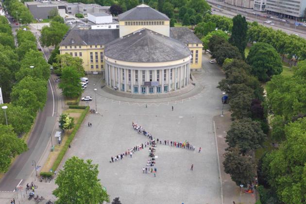 Ein Windrad aus Menschen auf einem Platz in Saarbrücken von oben fotografiert