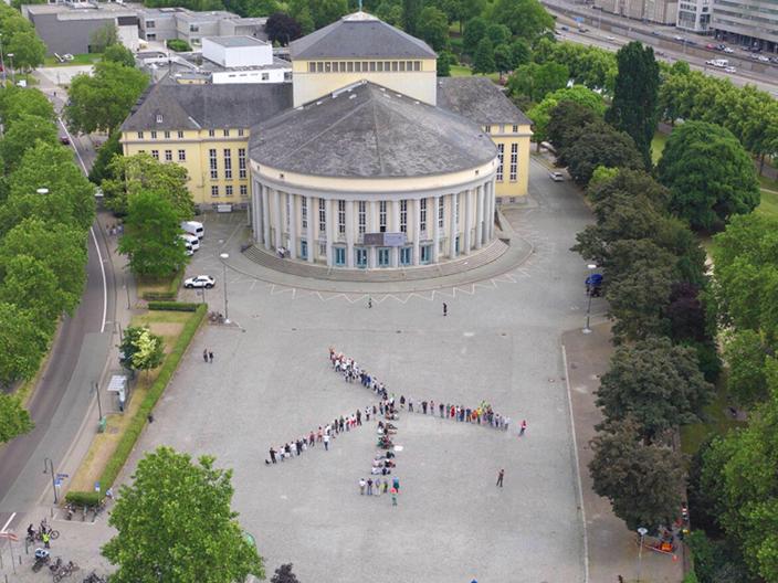 Ein Windrad aus Menschen auf einem Platz in Saarbrücken von oben fotografiert