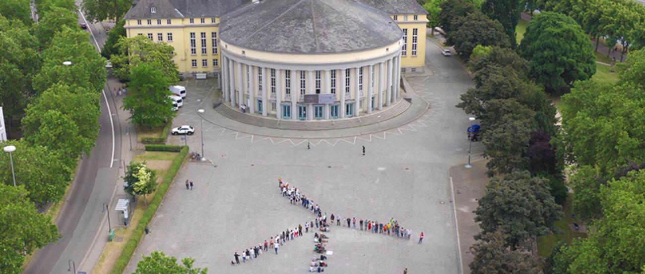 Ein Windrad aus Menschen auf einem Platz in Saarbrücken von oben fotografiert