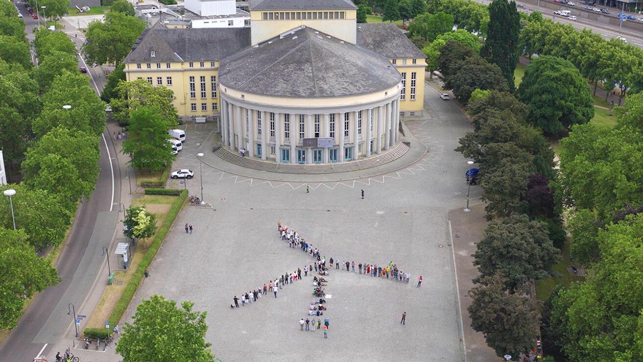 Ein Windrad aus Menschen auf einem Platz in Saarbrücken von oben fotografiert
