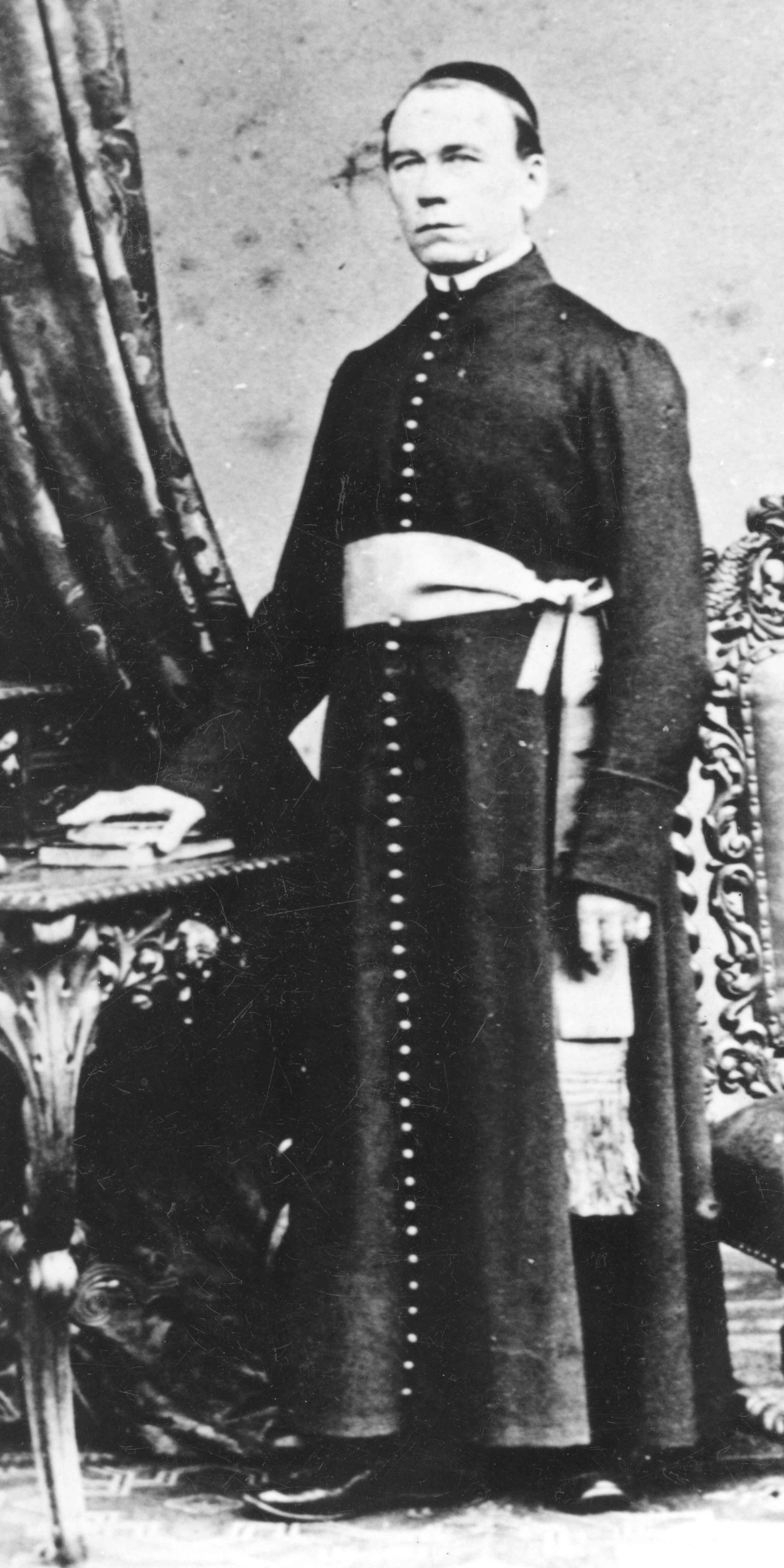 Das Bild zeigt Adolph Kolping gekleidet in Soutane stehend an einem Tisch.