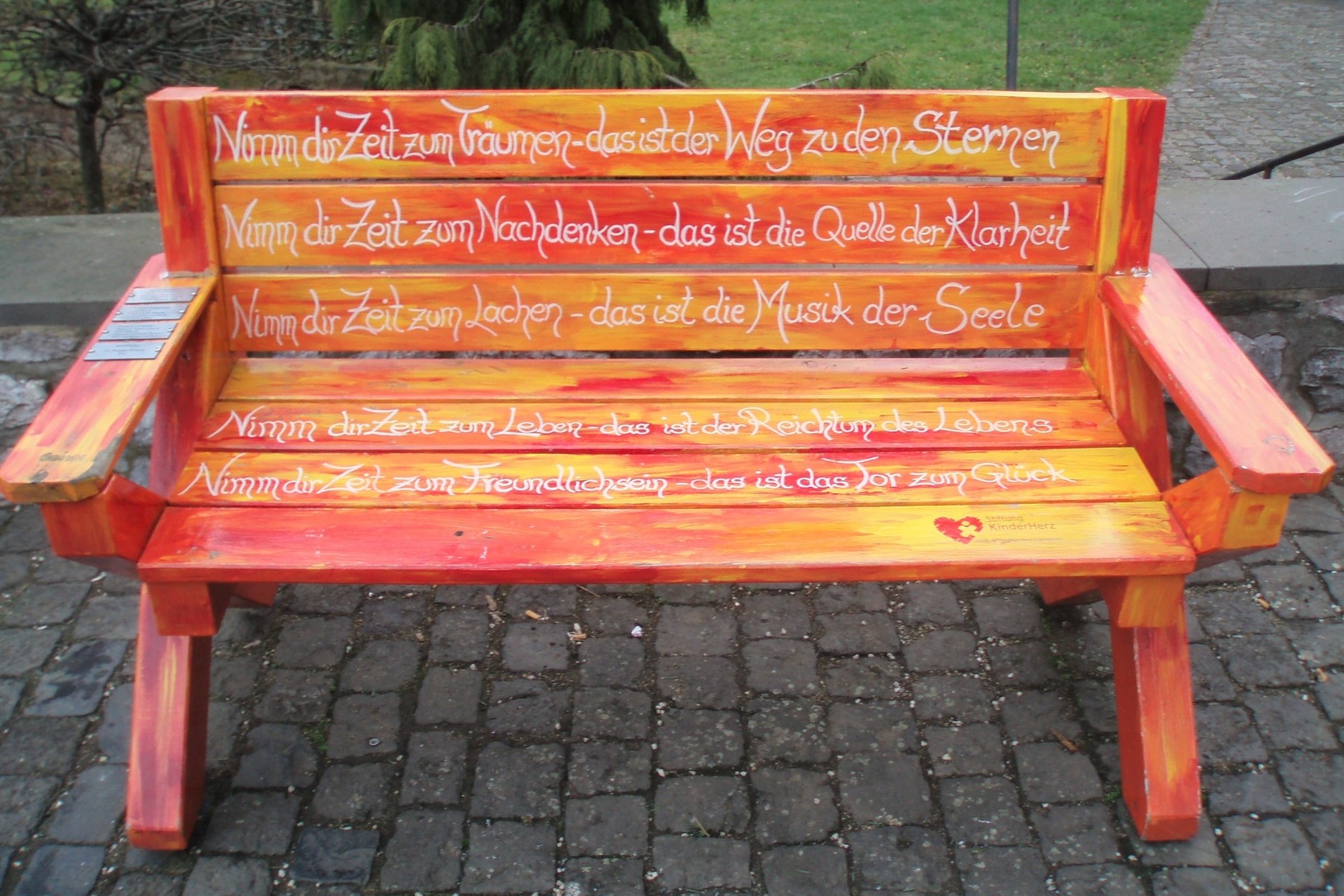 Eine bemalte Sitzbank in Orange- und Gelbtönen, darauf der Text nach einer irischen Weisheit: 'Nimm dir Zeit zum ...'