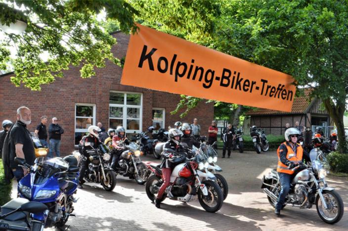 Motorradfahrer mit Motorrädern, dazu ein Plakat mit der Aufschrift: Kolping Biker Treffen