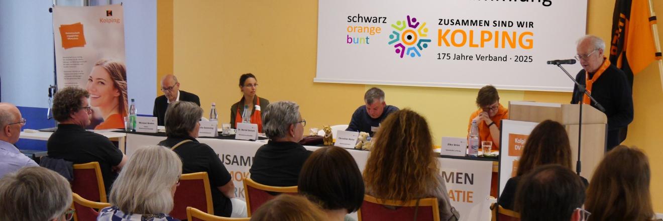 Delegierte einer Kolping-Versammlung schauen nach vorne auf den Vorstandstisch, ein Redner steht rechts am Pult.