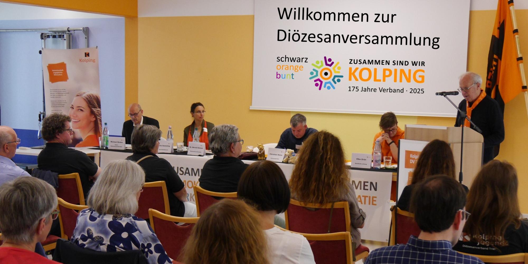 Delegierte einer Kolping-Versammlung schauen nach vorne auf den Vorstandstisch, ein Redner steht rechts am Pult.