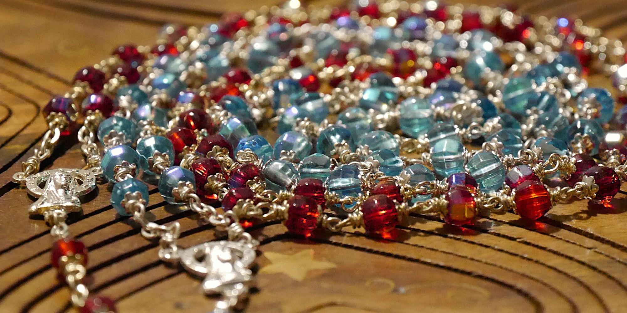 Eine rote und eine blaue Rosenkranz-Kette liegen spiralförmig auf einer Holzunterlage.
