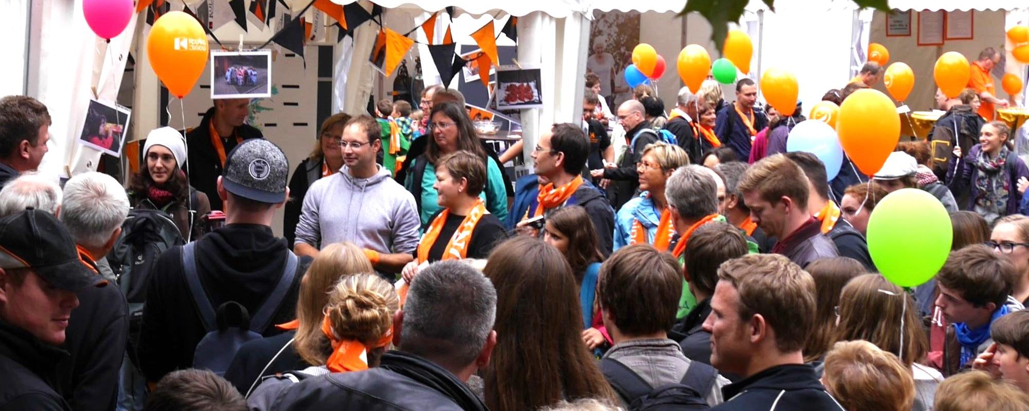 Man sieht eine Gruppe Menschen mit Kolpingschals und bunten Luftballons.