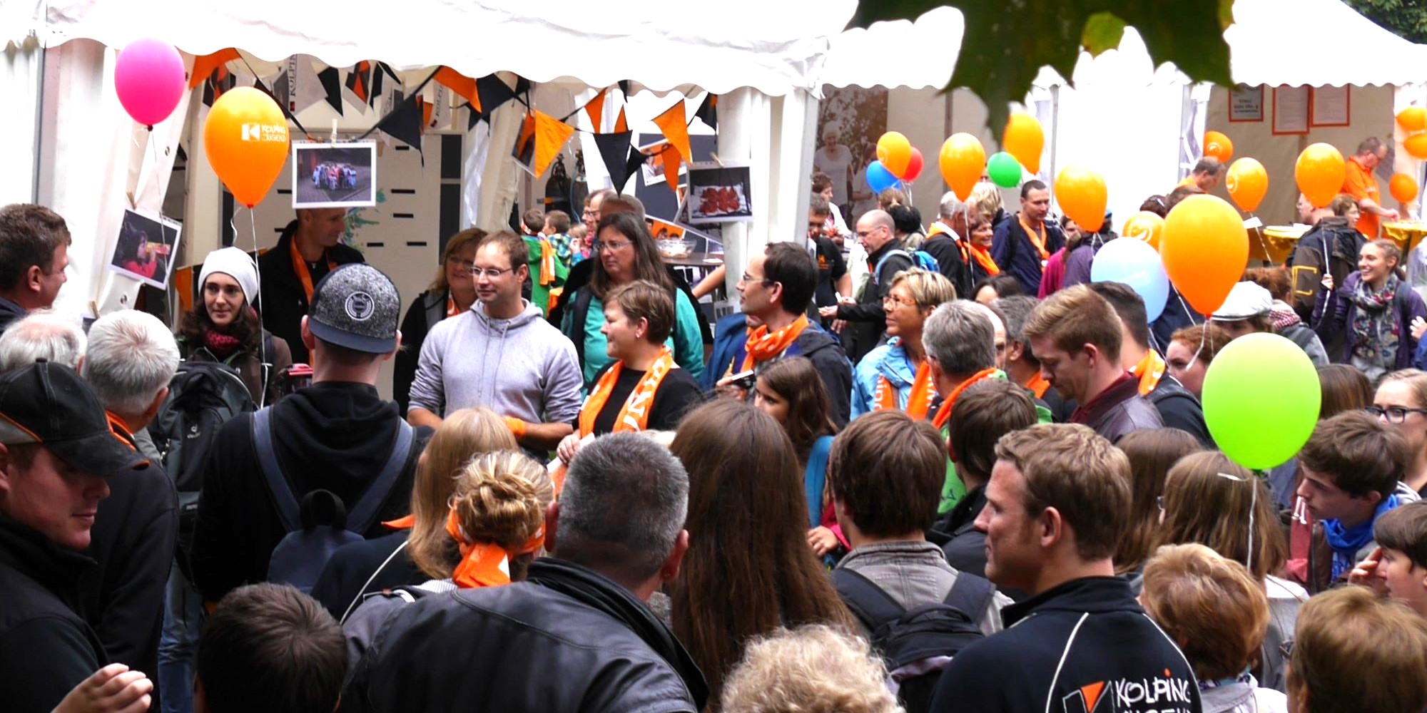 Man sieht eine Gruppe Menschen mit Kolpingschals und bunten Luftballons.