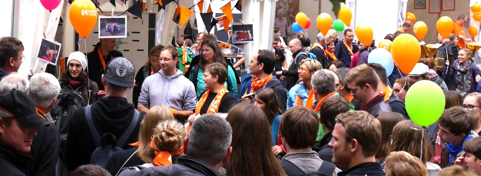 Man sieht eine Gruppe Menschen mit Kolpingschals und bunten Luftballons.