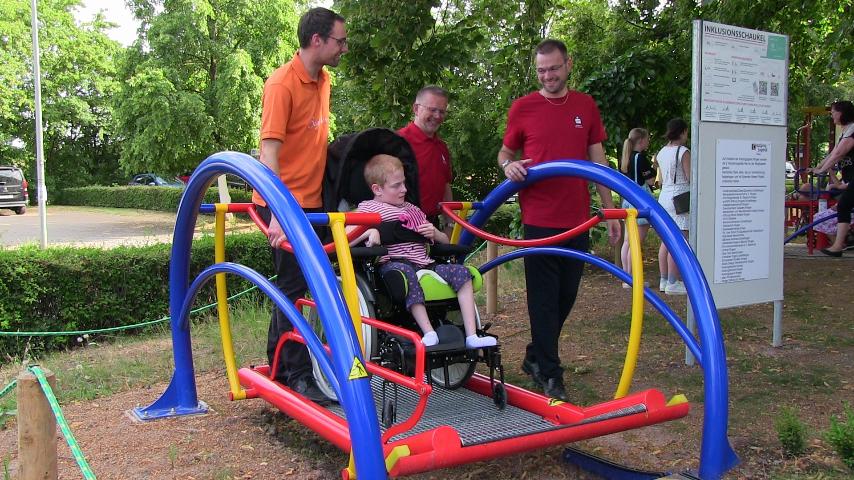 Einweihung einer Inklusions-Schaukel; drei Männer schneiden das Band durch