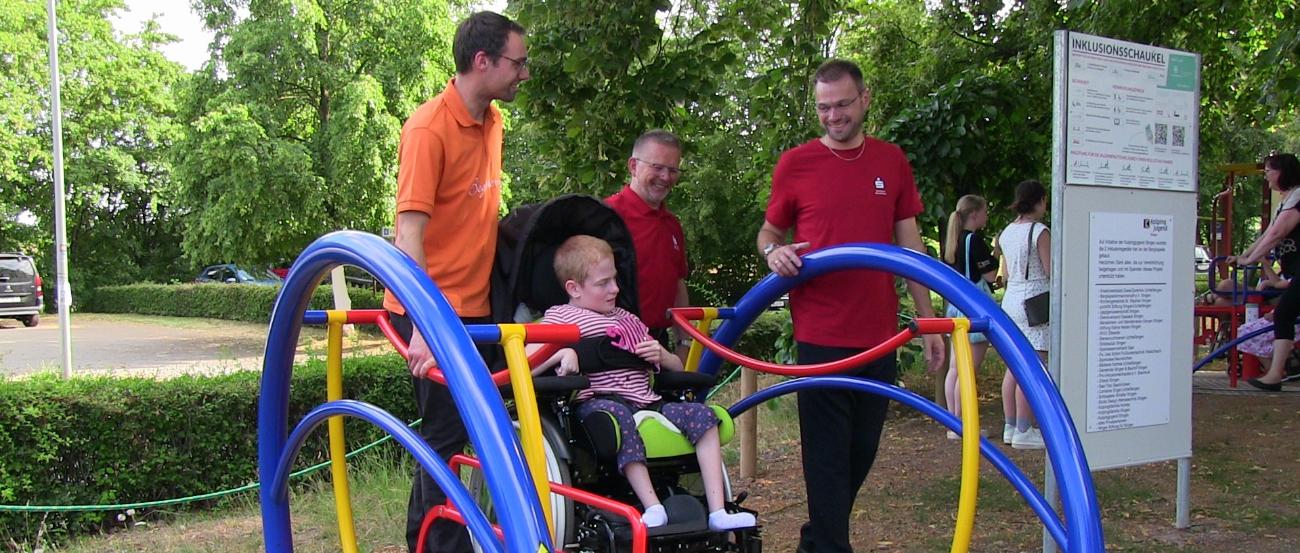 Einweihung einer Inklusions-Schaukel; drei Männer schneiden das Band durch