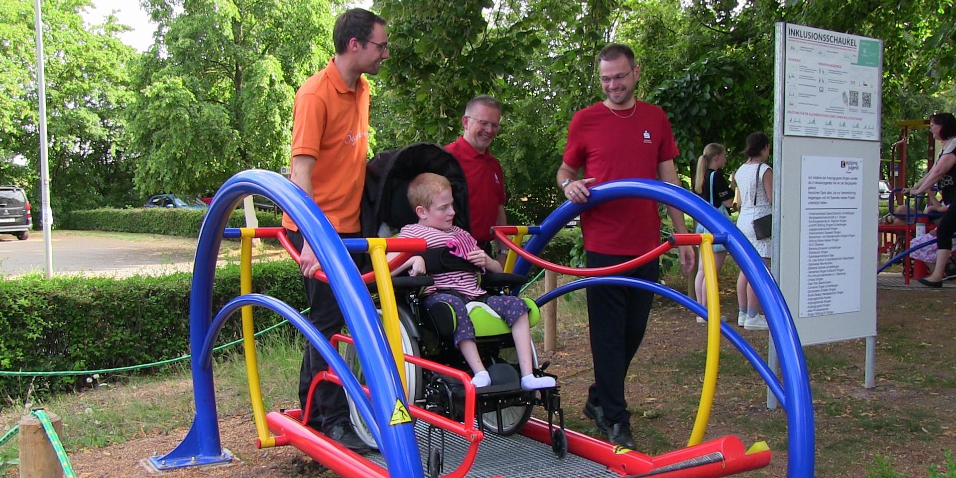 Einweihung einer Inklusions-Schaukel; drei Männer schneiden das Band durch