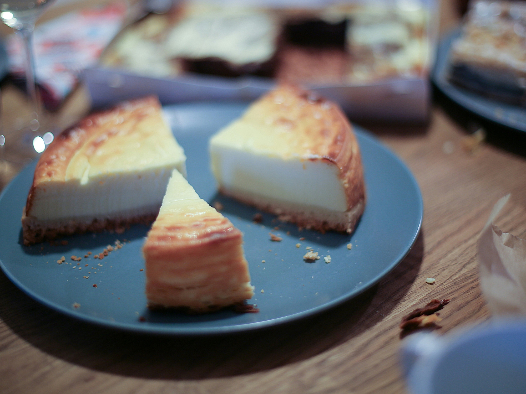 Auf einem Holztisch steht ein blauer Teller mit 3 Stücken Käsekuchen.