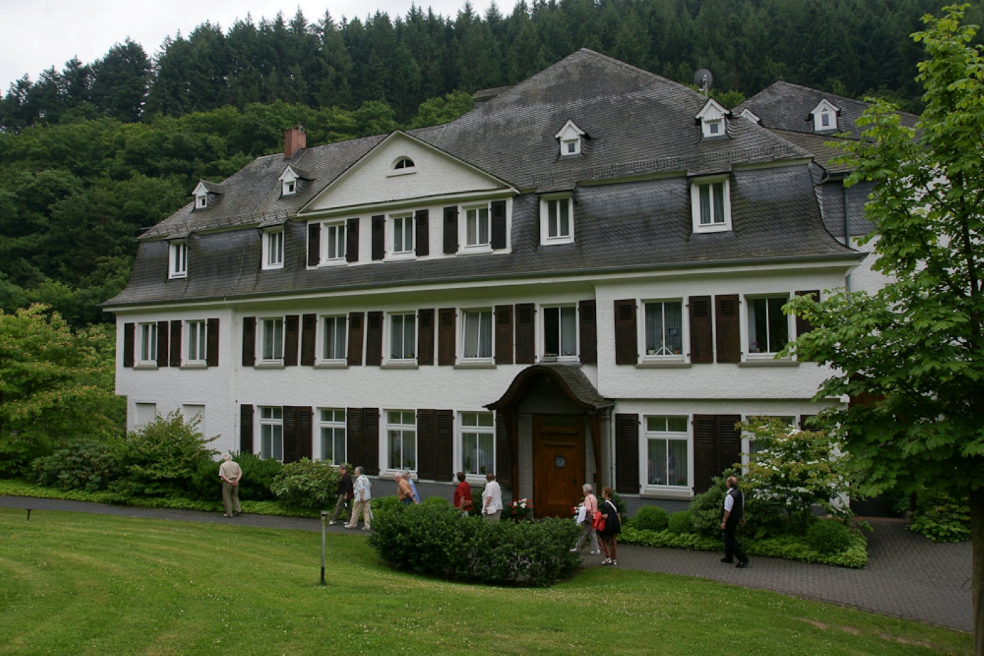 Klostergebäude umgeben von einem Garten und einem Waldhang im Hintergrund.