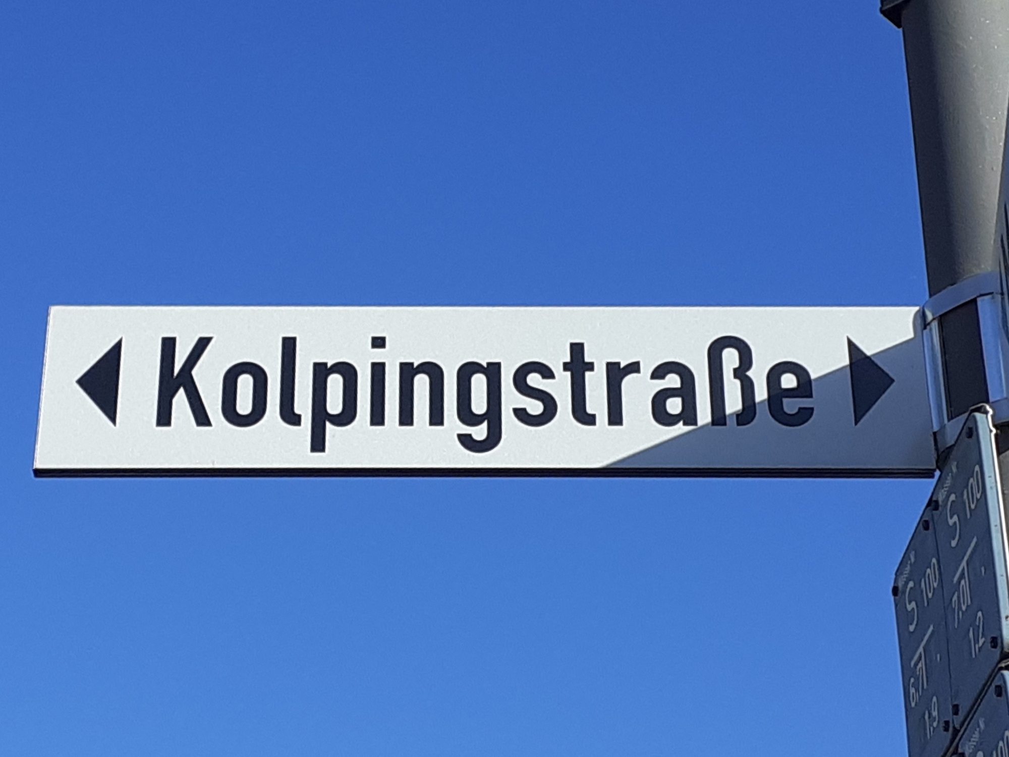 Das Bild zeigt ein Schild mit Aufschrift Kolpingstraße vor blauem Himmel.