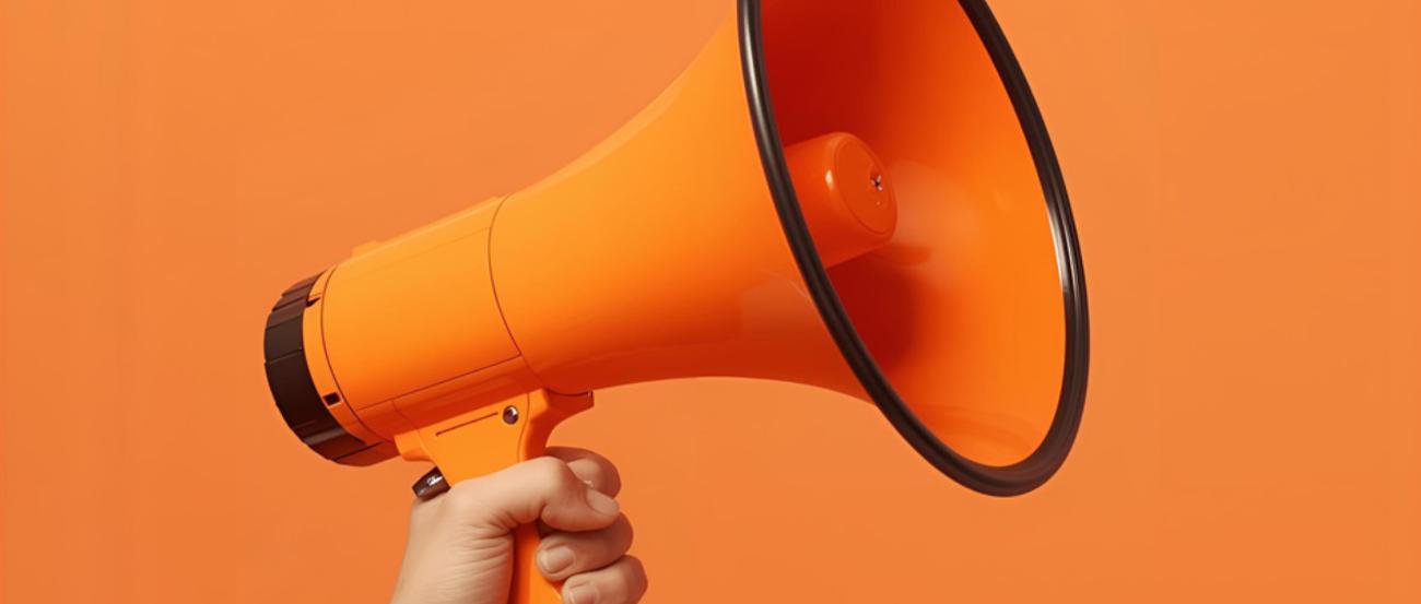 Megaphon mit orangenem Hintergrund (c) Kolpingwerk Trier Hand, die ein orangenes Megaphon in der Hand hält