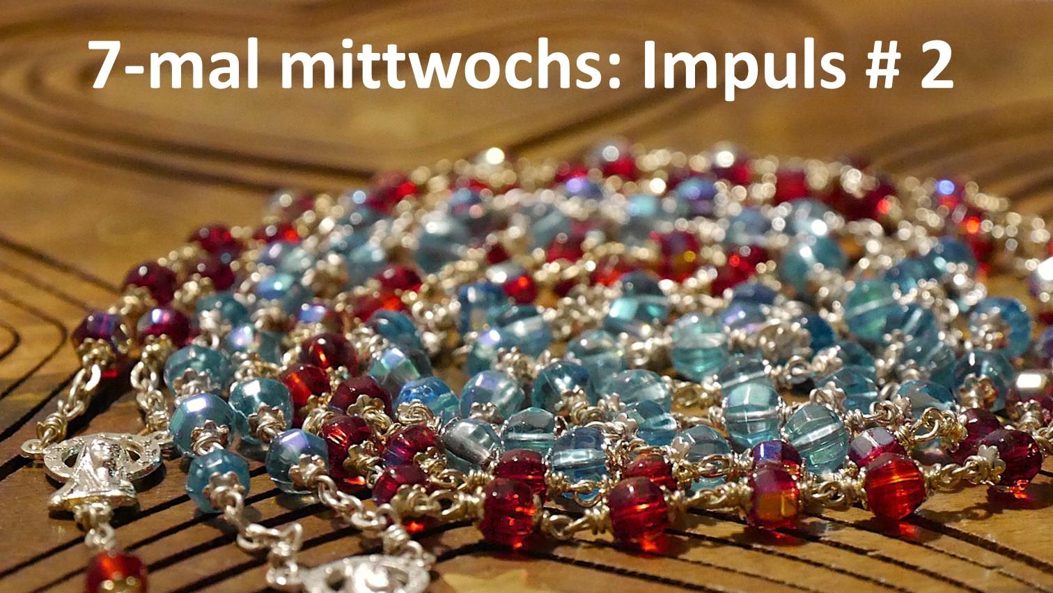 Eine rote und eine blaue Rosenkranz-Kette liegen spiralförmig auf einer Holzunterlage.