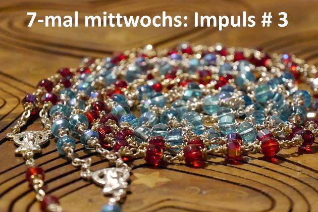 Eine rote und eine blaue Rosenkranz-Kette liegen spiralförmig auf einer Holzunterlage.