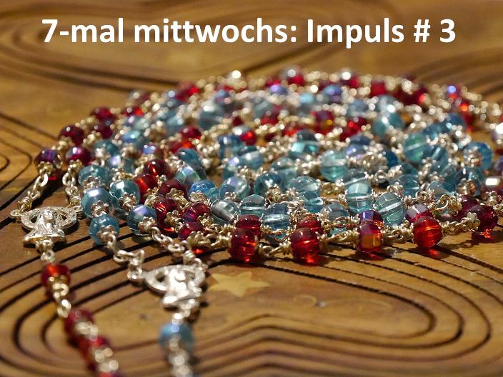 Eine rote und eine blaue Rosenkranz-Kette liegen spiralförmig auf einer Holzunterlage.