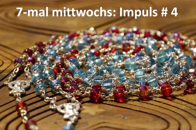 Eine rote und eine blaue Rosenkranz-Kette liegen spiralförmig auf einer Holzunterlage.