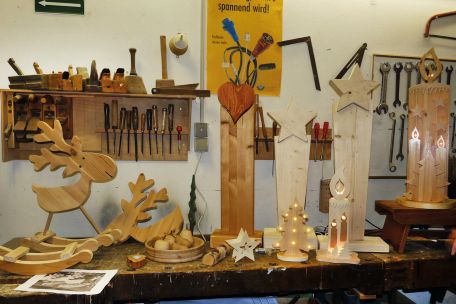Werkstücke aus Holz gefertigt werden auf einer Werkbank präsentiert, an der Wand dahinter hängen Regale mit Werkzeugen.