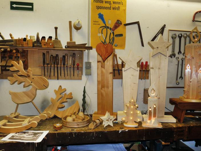 Werkstücke aus Holz gefertigt werden auf einer Werkbank präsentiert, an der Wand dahinter hängen Regale mit Werkzeugen.