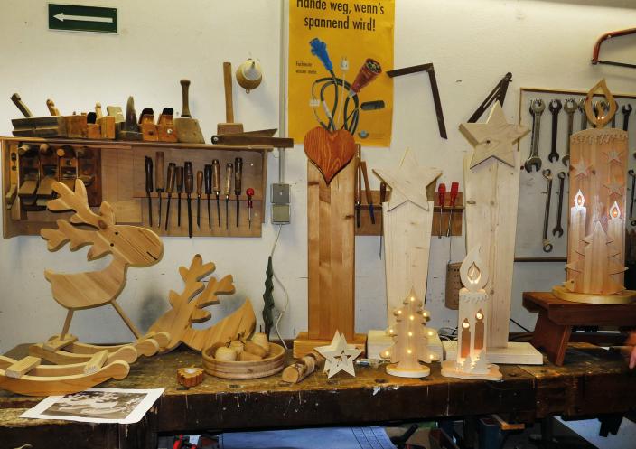Werkstücke aus Holz gefertigt werden auf einer Werkbank präsentiert, an der Wand dahinter hängen Regale mit Werkzeugen.