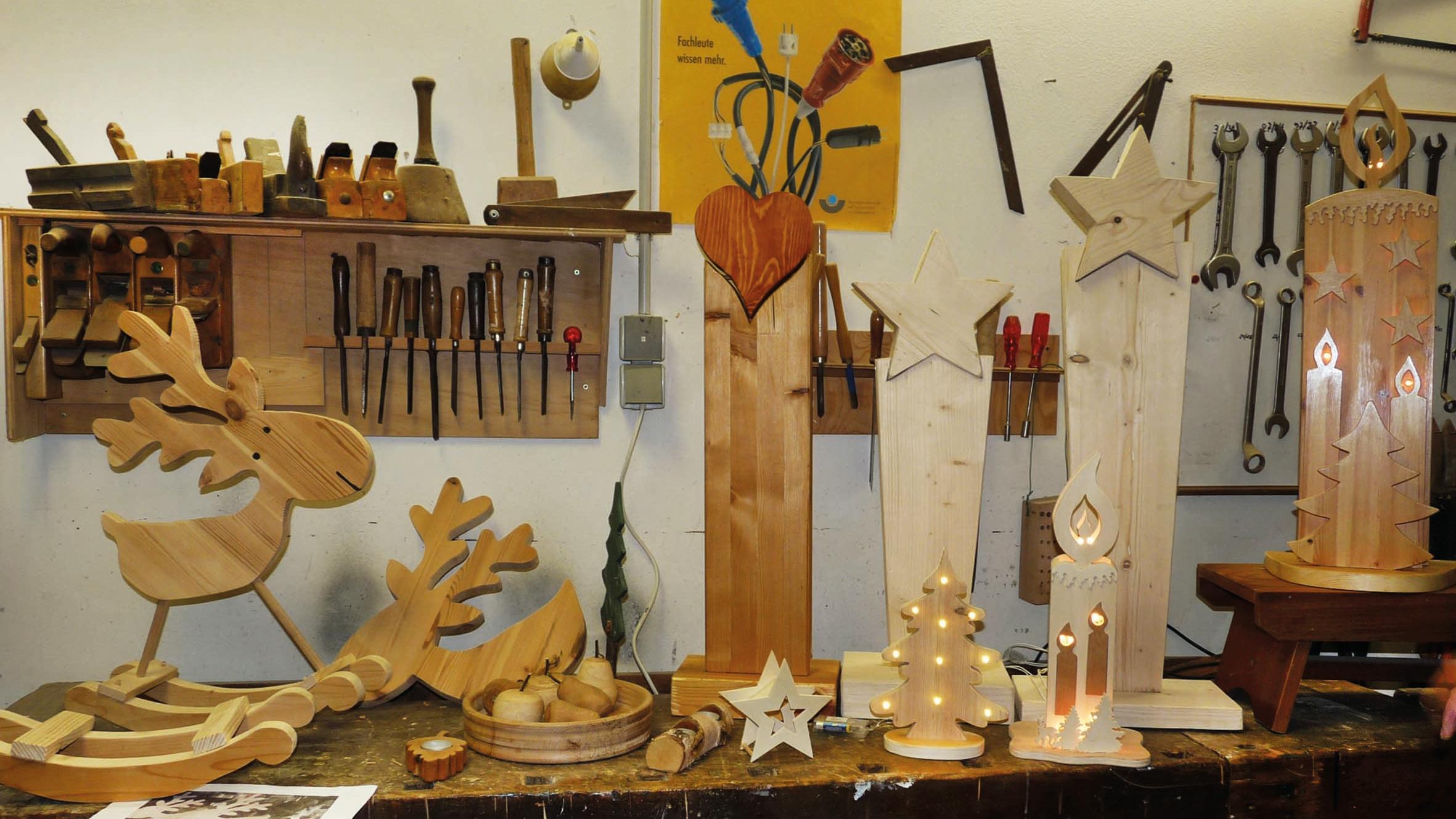 Werkstücke aus Holz gefertigt werden auf einer Werkbank präsentiert, an der Wand dahinter hängen Regale mit Werkzeugen.