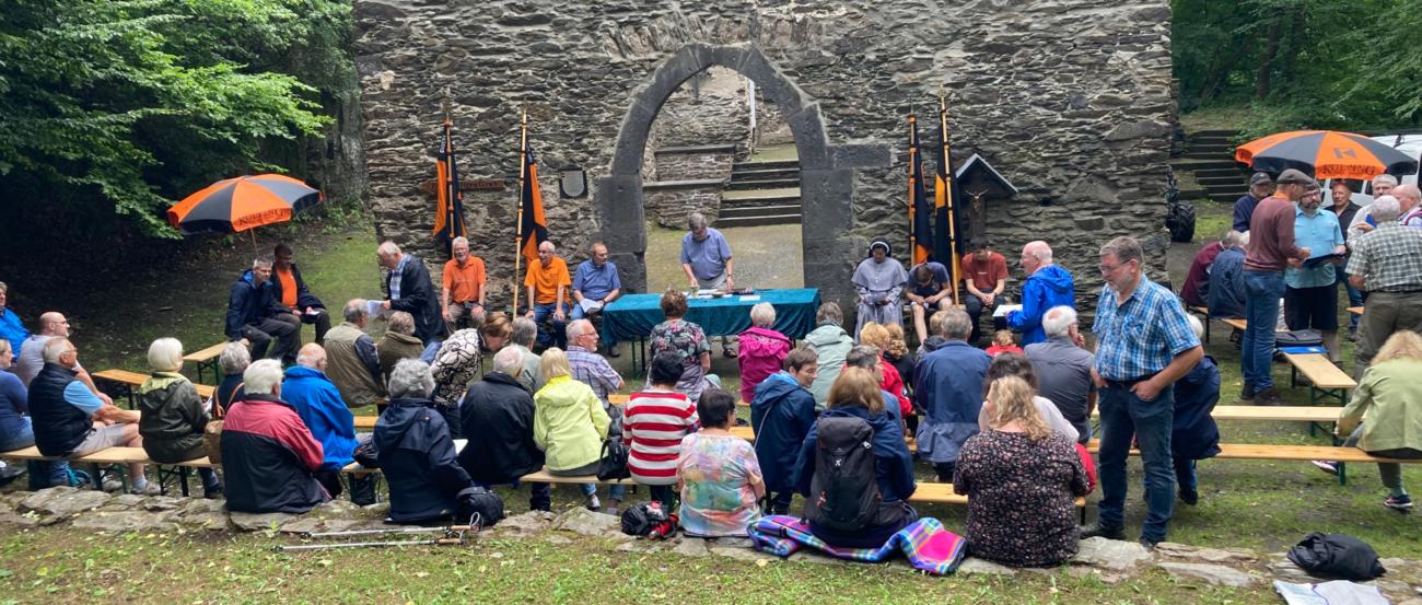 Menschen sitzen auf einer Wiese, im Hintergrund die Hausenborner Marienverehrungsstätte