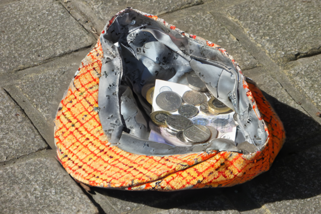 Man sieht eine Kappe oder Mütze auf dem Boden mit einigen Geldstücken darin